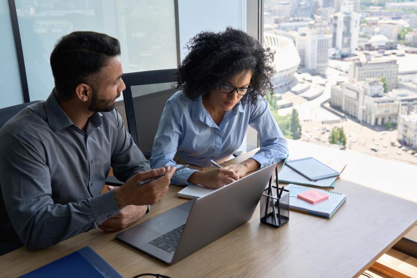 2 people sharing a desk, meeting in an office