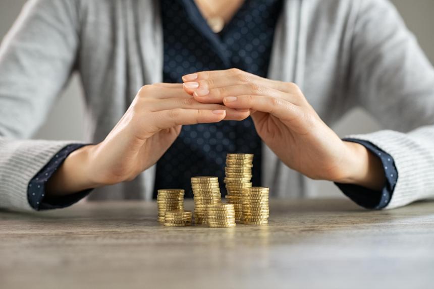 Hands crossed over stacks of gold coins to protect them